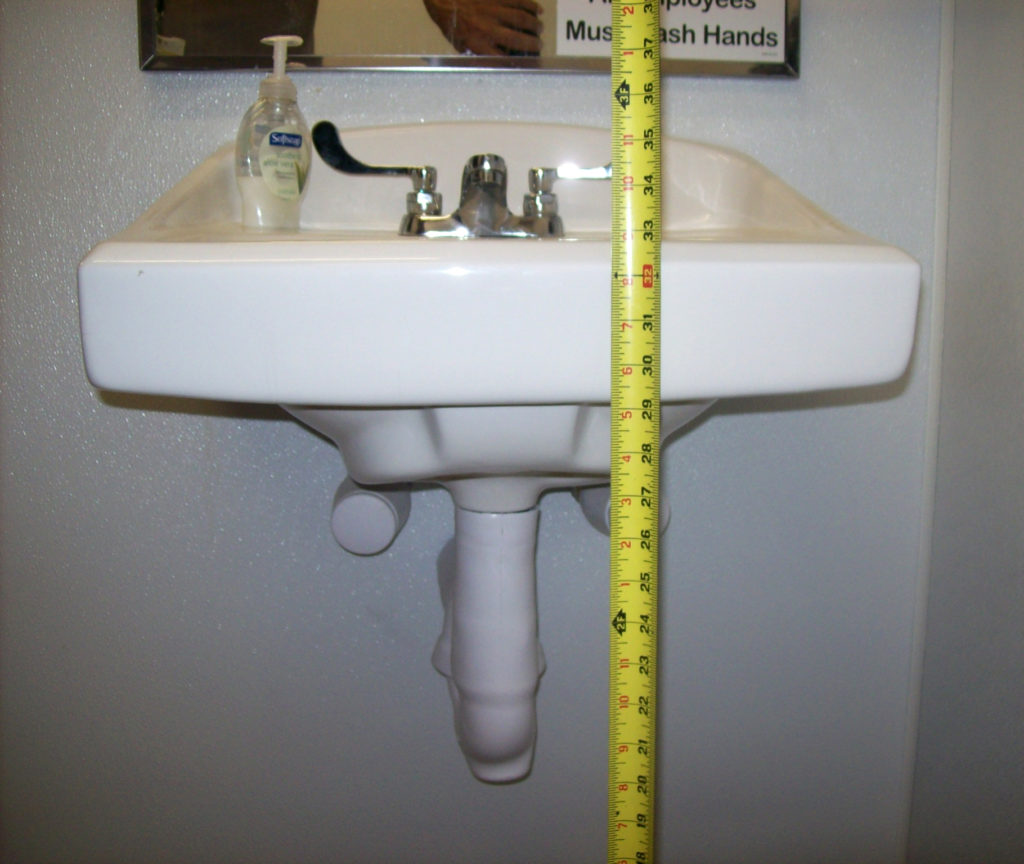 This is a photo of a lavatory in a restroom. Element compliance with ADA involves measuring for compliance.
For instance a lavatory has a maximum height of 34 inches to the top of the rim and must provide knee clearance at 27 inches. Handles shall be lever operated.
Pipes under the lavatory need insulated wrapping for protection from hot water.
Clear floor space of 30" x 48" inches is required at the lavatory, directly connected to maneuvering space within the restroom.
Question: Do YOU know if all of the elements in your restroom are compliant?